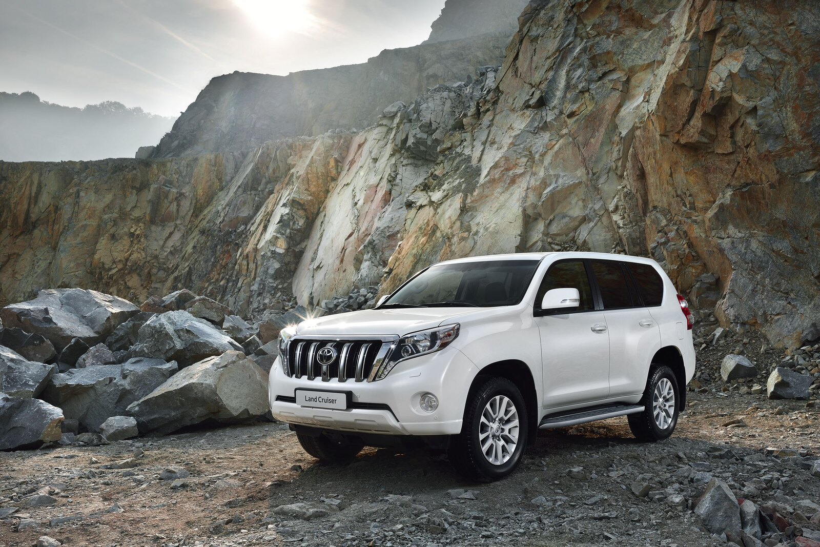 Белый Toyota Land Cruiser Prado у скальной стены на грунтовой дороге